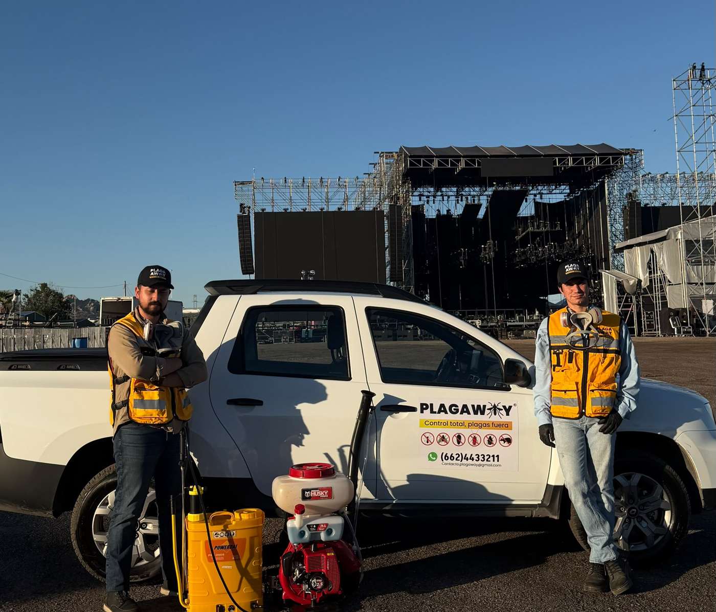 Dos técnicos de Plagaway junto a la camioneta de la empresa frente al escenario de un evento masivo