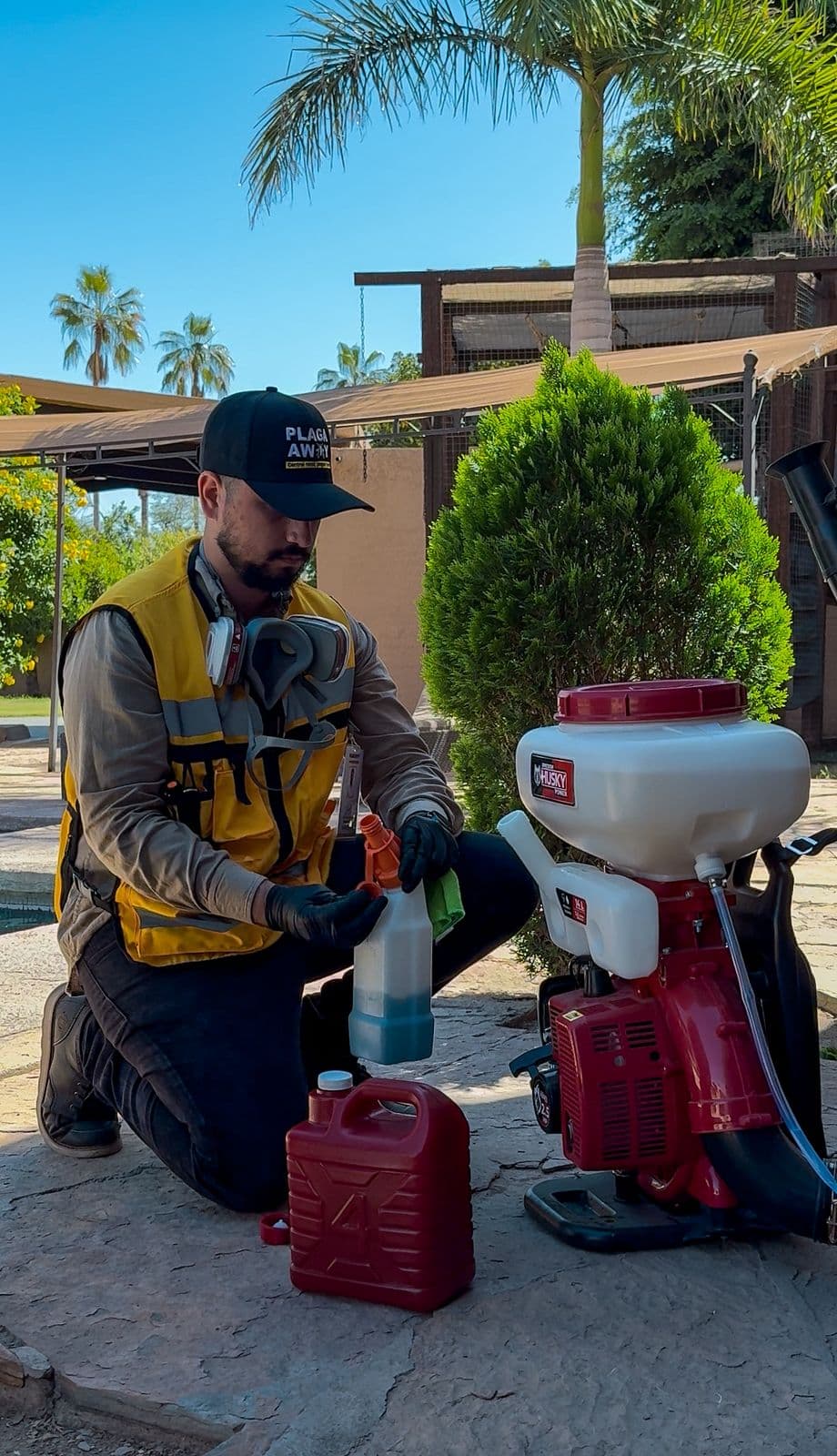Técnico de Plagaway arrodillado midiendo y preparando la dosis de producto junto a la bomba motorizada y un bidón en un jardín